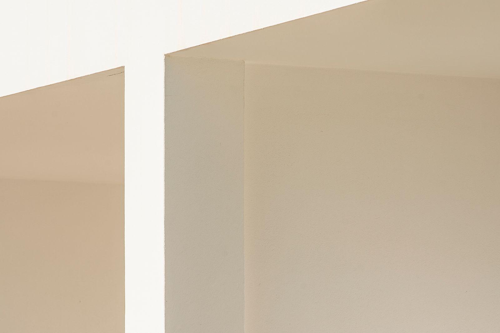 Pale architectural plaster planes meet in a softly lit corner