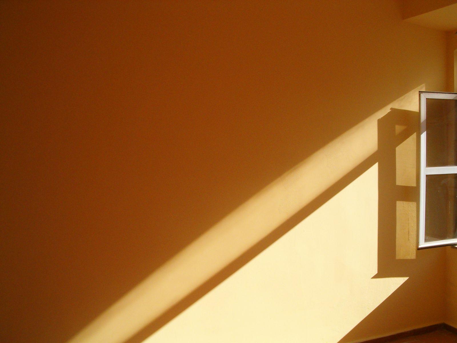 Afternoon sunlight falls diagonally across a warm ochre plaster wall beside an open window